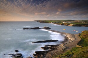 A coastal landscape with rocky cliffs, a pebble beach, and a village in the background. - Scandinavian Cabin near Bude with Log Burner (Kilkhampton)
