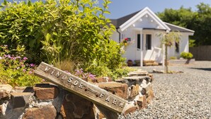 A wooden sign with the text "VINDORS FARM" on a stone wall, with a white building and greenery in the background. - Scandinavian Cabin near Bude with Log Burner (Kilkhampton)