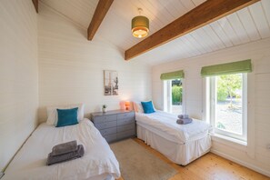 Une chambre avec deux lits, une commode, une lampe et une fenêtre donnant sur un paysage verdoyant.