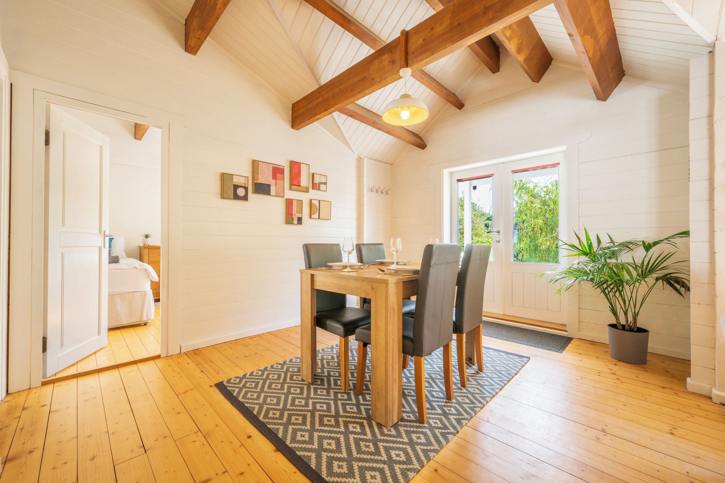 Un espace repas comprenant une table et des chaises en bois, un tapis à motifs et un plafond avec des poutres apparentes.