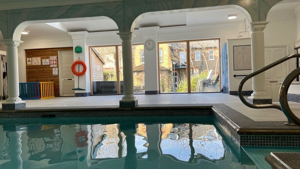 Una piscina interior con paredes de vidrio transparente, un flotador salvavidas y un reloj en la pared.