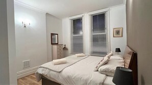 Un dormitorio con cama, mesita de noche, lámpara, cómoda y persianas.