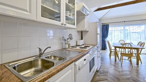 Una cocina con un lavamanos doble, estufa y comedor con sillas de madera.