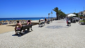 Een verharde promenade met banken, palmbomen en strandparasols.