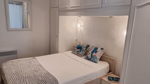A bedroom with a bed, a bedside table, a nightstand, a window with curtains, and a wall-mounted light fixture. - Holiday one bedroom apt, in heart of old town, lovely sea view (Villefranche-Sur-Mer)