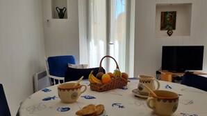 A dining area with a table set for breakfast, including cups, a basket of fruit, and a plate of biscuits. - Holiday one bedroom apt, in heart of old town, lovely sea view (Villefranche-Sur-Mer)