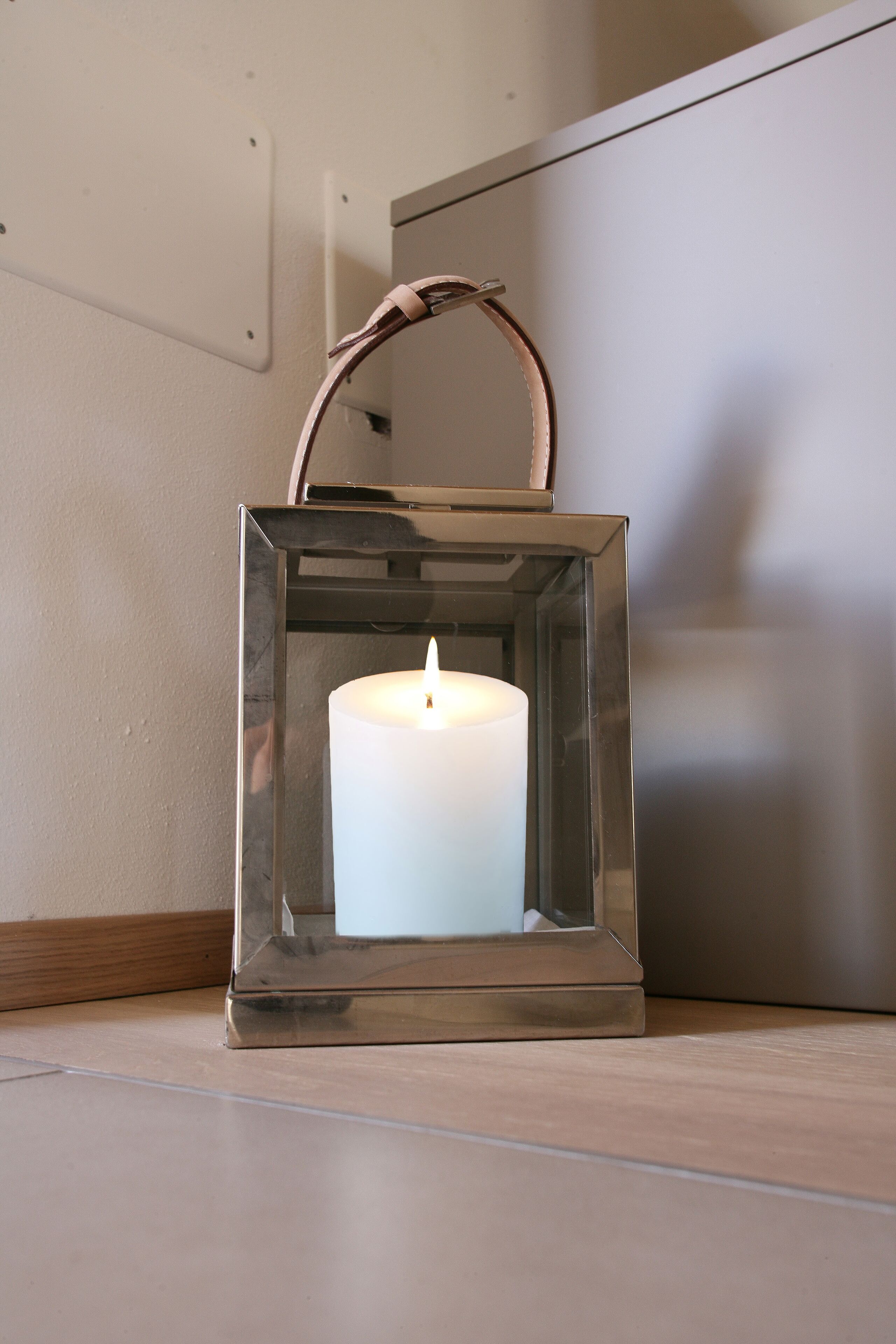 A candle in a clear glass lantern on a wooden floor.