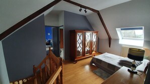 A bedroom with a sloped ceiling, a wooden wardrobe, a bed with a grey bedspread, and a window with a view. - Country Cottage / Gite - SAINT GOUENO (Le Mené)