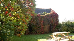 A picnic table in a garden with a wooden fence and a building covered in ivy. - Country Cottage / Gite - SAINT GOUENO (Le Mené)