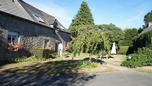 A stone house with a sloped roof, a garden with flowers, and a tall tree. - Country Cottage / Gite - SAINT GOUENO (Le Mené)