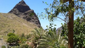 A mountainous landscape with a prominent rocky peak, lush greenery, and a small building with a red roof. - Enjoy Casa Rural La Tinta (Buenavista del Norte)