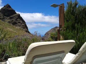 A beachside view with a mountain in the background, a wooden post with a solar panel, and two beige lounge chairs. - Enjoy Casa Rural La Tinta (Buenavista del Norte)