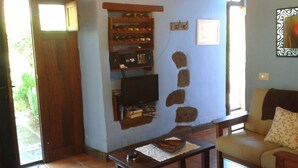 A living room with a TV, a bookshelf, a stone wall decoration, a sofa, and a dining table. - Enjoy Casa Rural La Tinta (Buenavista del Norte)