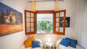 A small room with two beds, a window with curtains, a small table, and a painting on the wall.