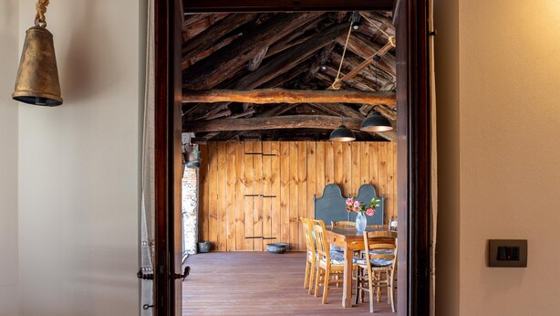 A wooden interior with a dining area, a hanging light fixture, and a door leading to another room.