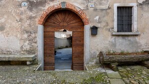 An arched wooden door with a brick archway, a small window with a metal grid, and a stone bench outside.