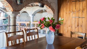 A wooden table with a vase of flowers, surrounded by chairs, in a rustic setting with exposed brick arches and wooden walls.