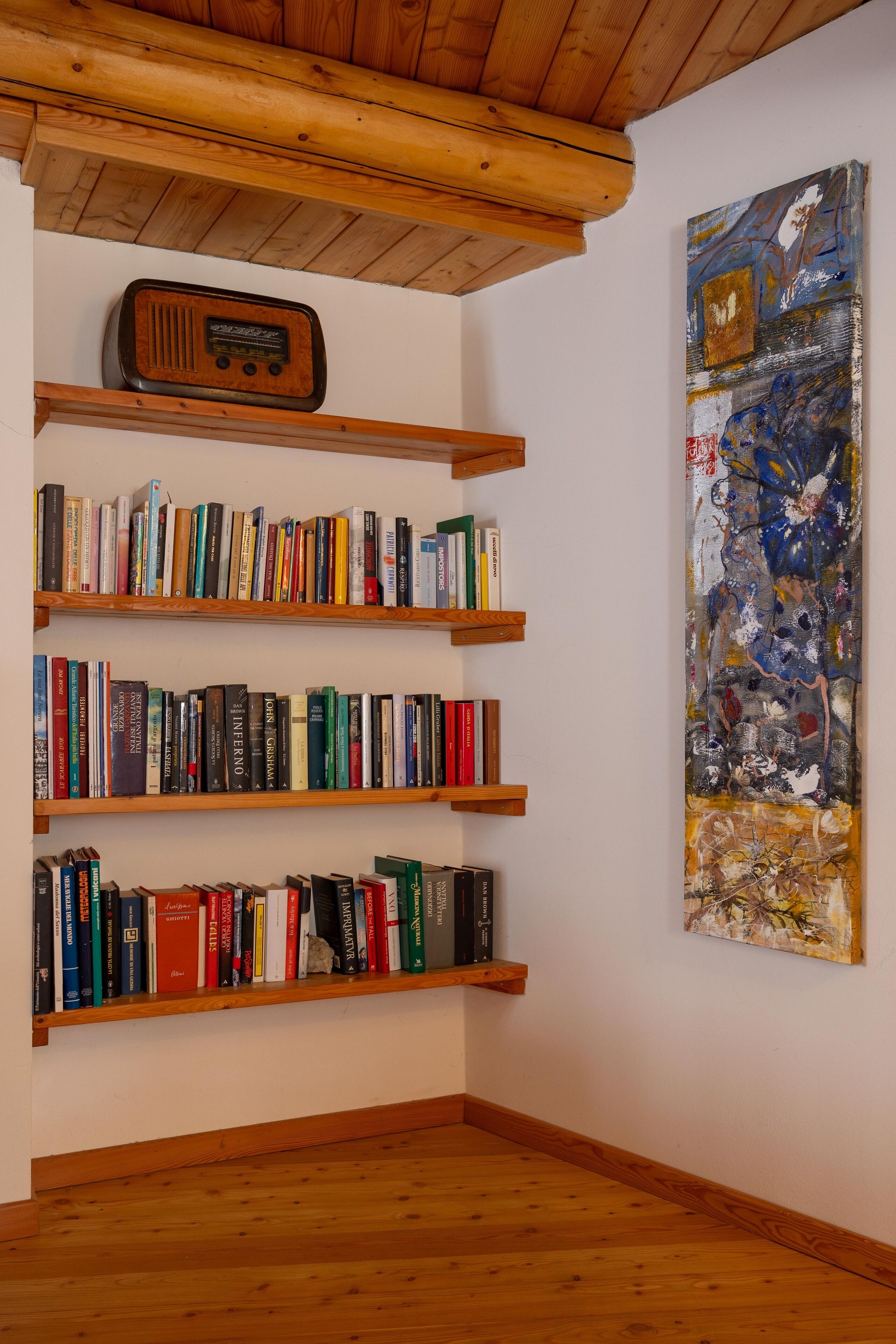 A room with wooden bookshelves filled with books, a wooden ceiling, and a large abstract painting on the wall.