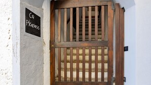 A wooden gate with vertical bars, a stone staircase, and a sign that reads "Co Dolciass".