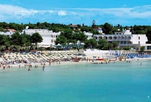 A beach with white buildings, trees, and people.