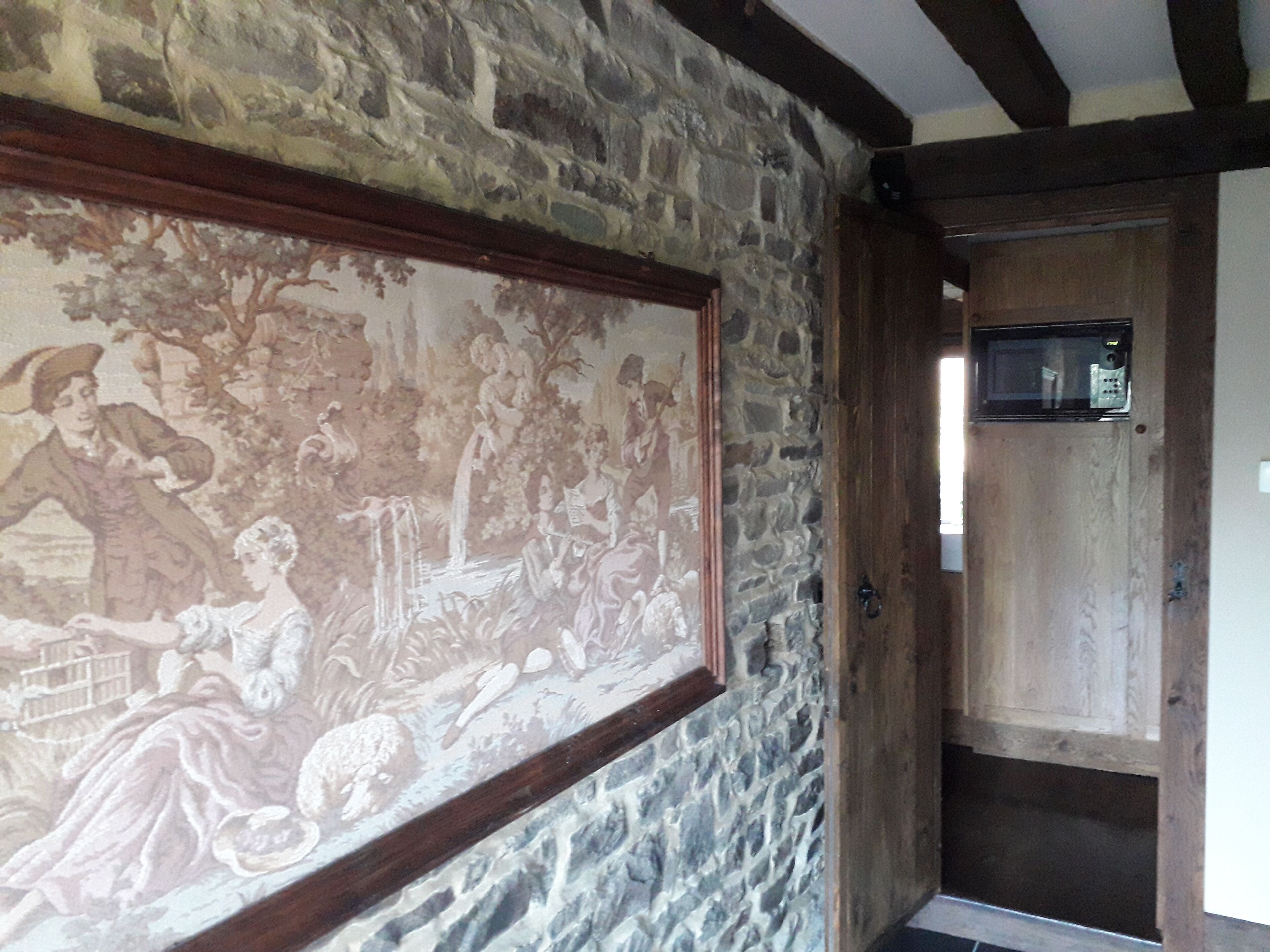 Quarto com parede de pedra, uma pintura histórica emoldurada e porta de madeira com um micro-ondas em cima.