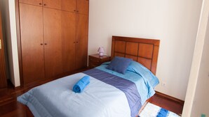 Een slaapkamer met een grote houten garderobe, een bed met blauw beddengoed en een nachtkastje met een lamp.