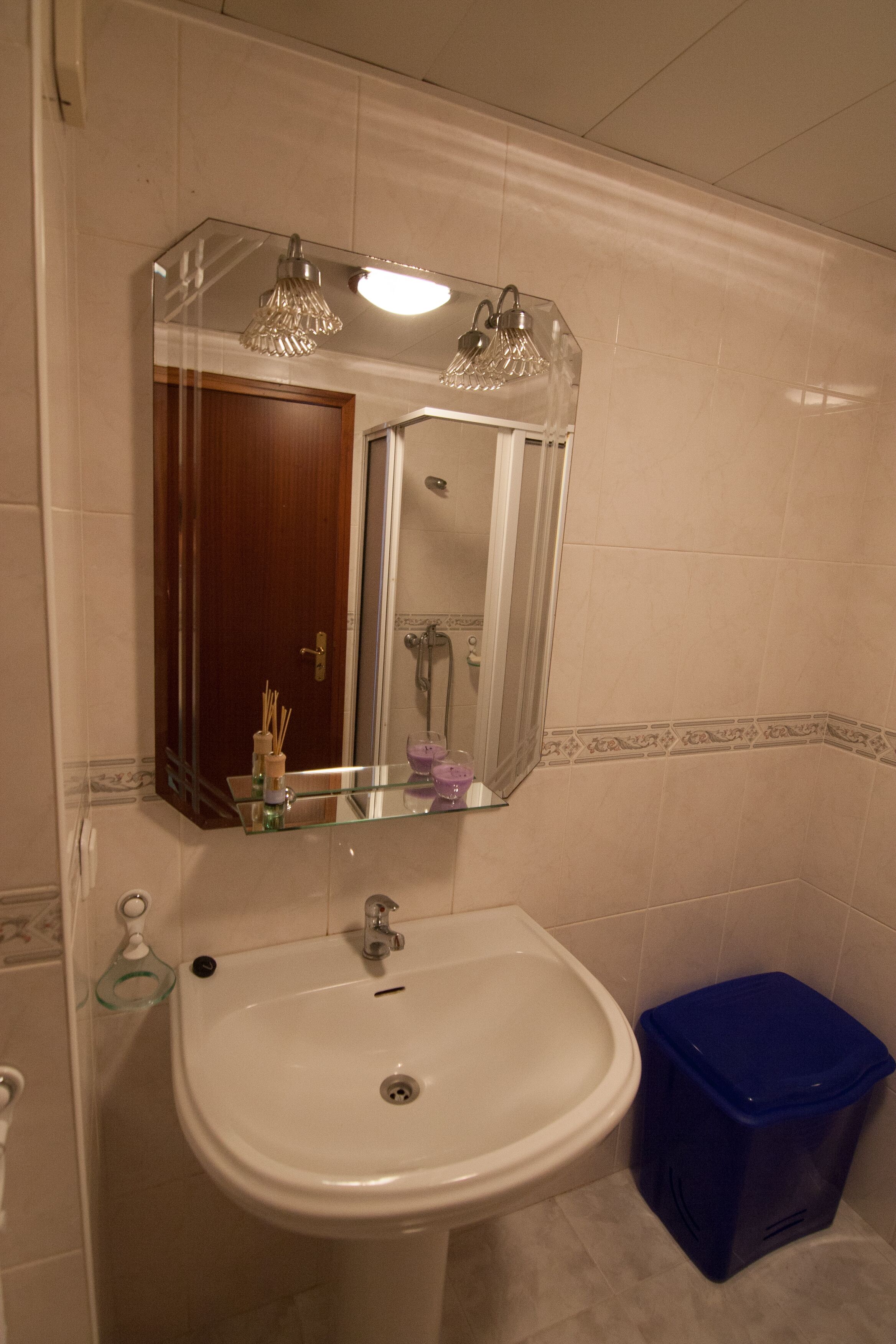 Un baño con un lavabo blanco, un espejo y un cubo de basura azul.