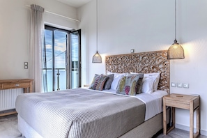 Ein Schlafzimmer mit einem großen Bett, einem Holz-Kopfschild, zwei Nachttischen, einem Fenster mit Vorhängen und Blick zum Himmel.