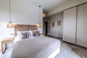 A bedroom with a large bed, two bedside tables, a wardrobe, and a door leading to another room.