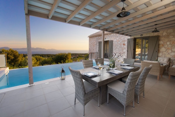 A dining area with a pool view, outdoor furniture, and a stone building.