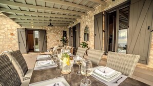 Un espacio de comedor al aire libre con paredes de piedra, muebles de mimbre y una mesa lista para una comida.