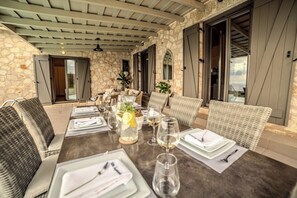 An outdoor dining area with stone walls, wicker furniture, and a table set for a meal.