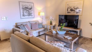 Una sala de estar con un sofá, una mesa de centro, un televisor y dos cuadros en la pared.