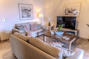 A living room with a sofa, a coffee table, a TV, and two framed artworks on the wall.
