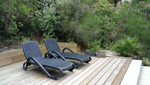 Deux fauteuils de jardin sur une terrasse en bois, avec un jardin en arrière-plan.