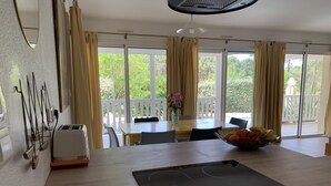 Eine moderne Küche mit integriertem Induktionskochfeld, einem Esstisch mit Stühlen und Blick ins Freie durch große Fenster.