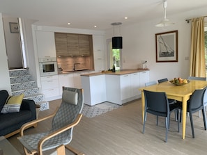 A modern kitchen with white cabinetry, a central island, and a dining area with a wooden table and chairs. - House / Villa - Lacanau Océan (Lacanau)