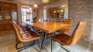 A dining area with a long wooden table and leather chairs, stone walls, and hanging pendant lights.
