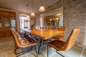 Uma sala de jantar com uma mesa de madeira comprida e cadeiras de couro, paredes de pedra e luminárias pendentes.
