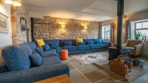 A cozy living room with a stone wall, a blue sofa set, a wooden coffee table, a fireplace, and a large window.