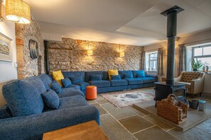 Uma sala de estar aconchegante com parede de pedra, sofá azul, mesa de centro de madeira, lareira e uma janela grande.