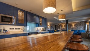 A modern kitchen with a large island, bar stools, and a stone accent wall.