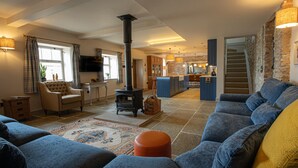 A cozy living room with a large blue sofa, a small round orange ottoman, and a traditional fireplace.