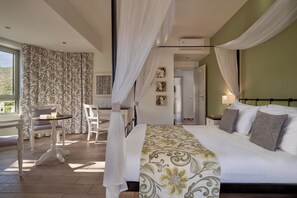 Un dormitorio con cama, un escritorio y una silla. Se ve una ventana con cortinas, una puerta y una pared con cuadros enmarcados.