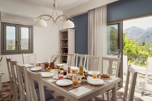 A dining area with a table set for breakfast, a bookshelf, and a view of the outdoors. - Alonia Villa, Refined Living with 50m² Private Pool (Rethymno)