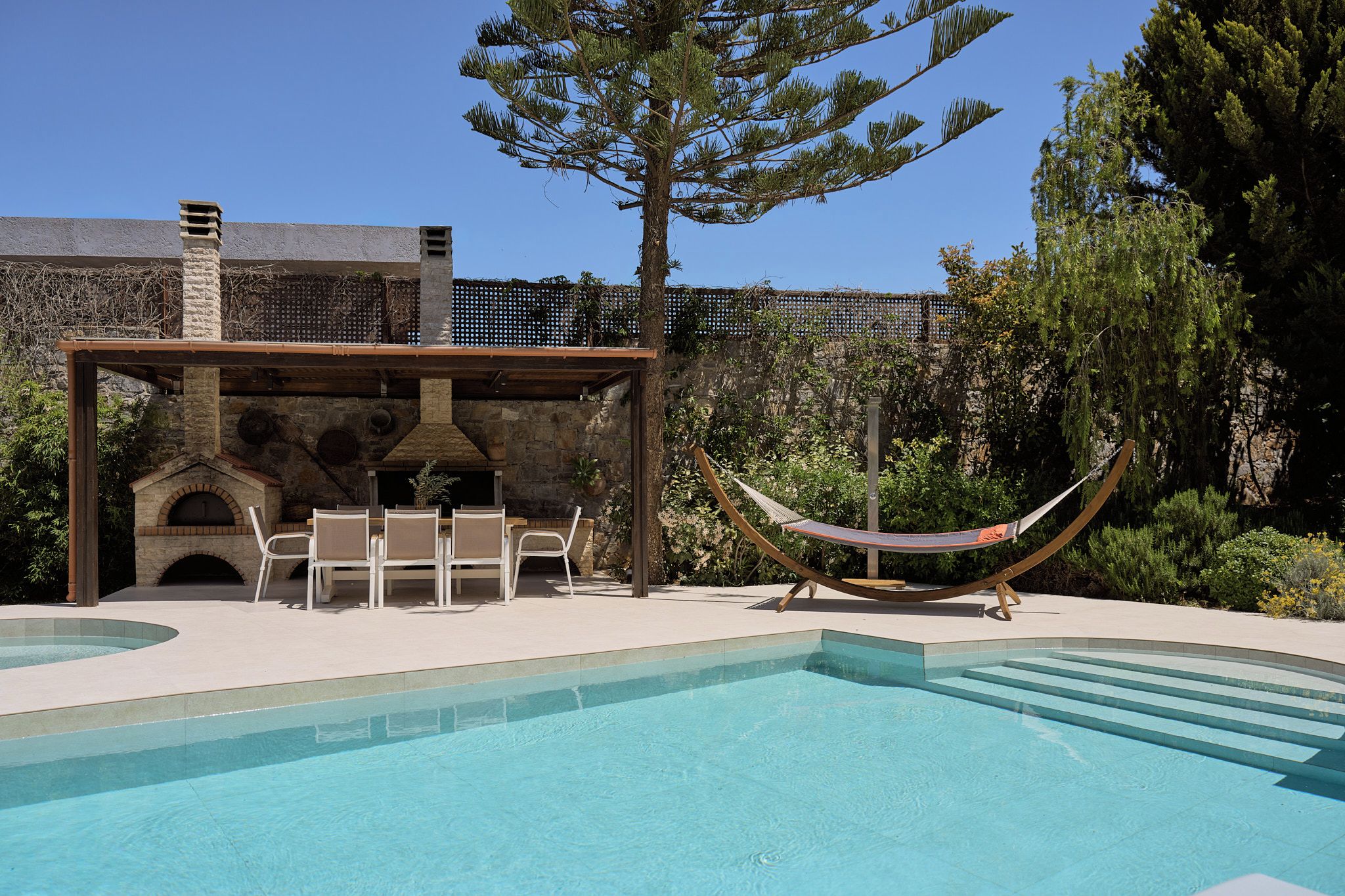 Ein Pool mit einer Steinstruktur, Sitzgelegenheiten im Freien und einer Hängematte.