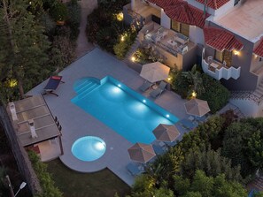 Una piscina con un jacuzzi integrado, rodeada de sillones y sombrillas.