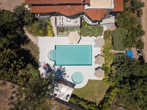 An aerial view of a property with a large swimming pool, a tennis court, and a covered patio area.