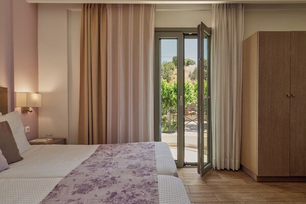 A hotel room with a bed, a nightstand, a lamp, a wardrobe, and a sliding glass door leading to an outdoor area.