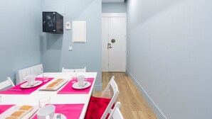 Zona pranzo con tavolo bianco imbandito per quattro persone, sottopiatti rosa e sedie bianche.